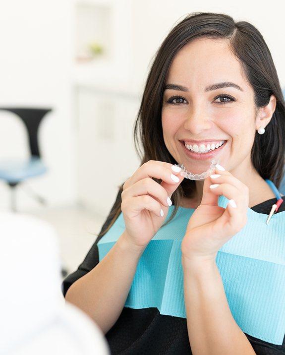 Smiling patient holding clear aligner