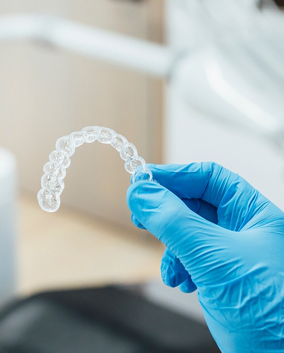 Dentist with blue glove holding clear aligner