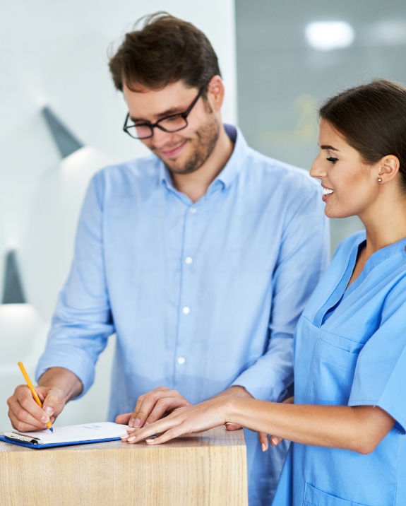 Man filing out form on clipboard at dental office front desk